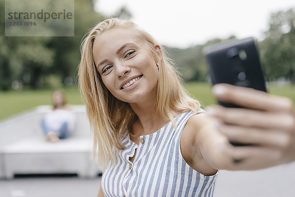 Porträt einer lächelnden jungen Frau  die einen Selfie in einem Skatepark nimmt.