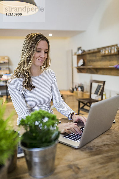 Lächelnde Frau mit Laptop auf Holztisch zu Hause