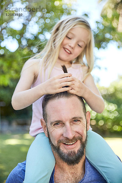 Ein glückliches Mädchen  das auf Vaters Schultern sitzt und seine Haare macht.