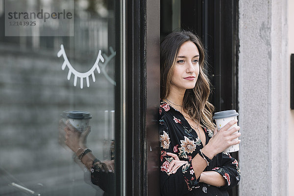 Porträt einer modischen Frau mit Kaffee zum Mitnehmen an der Eingangstür ihres Ladens