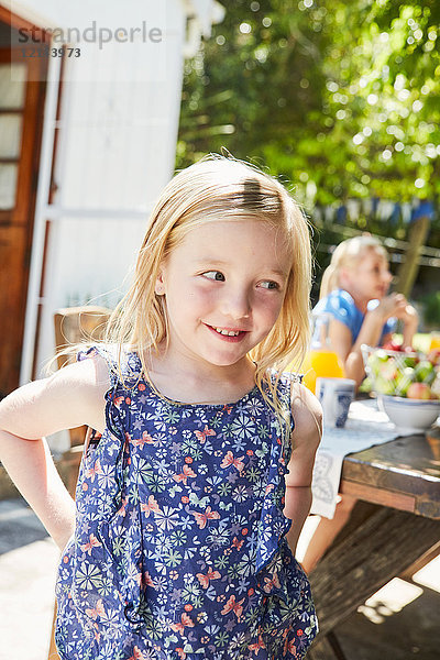 Porträt des lächelnden Mädchens mit Mutter im Hintergrund am Gartentisch