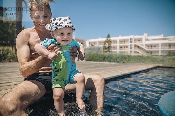 Vater und Sohn testen Wasser im Schwimmbad während der Sommerferien