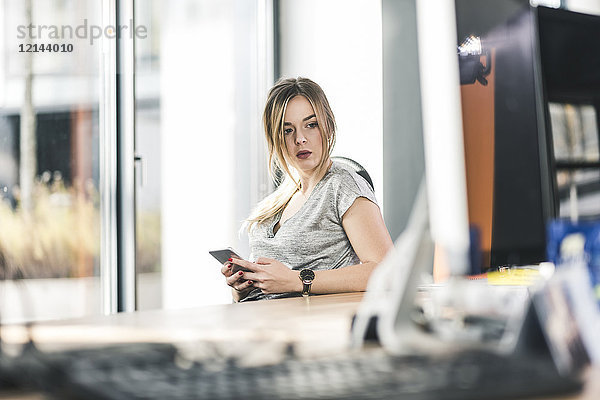 Geschäftsfrau mit Handy am Schreibtisch im Büro