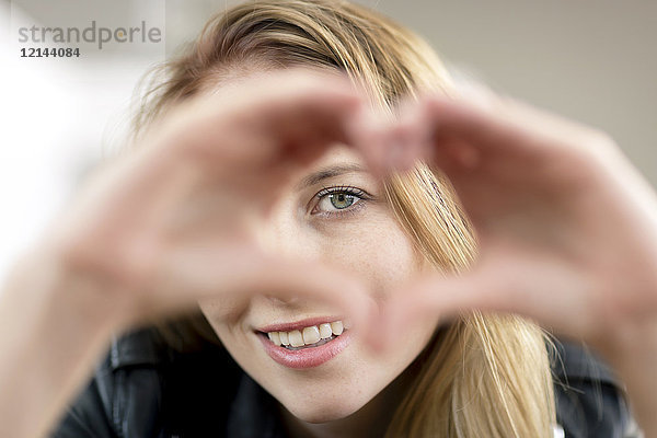 Porträt einer lächelnden jungen Frau  die mit ihren Händen das Herz formt.