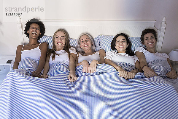 Porträt von glücklichen Freundinnen im Bett nebeneinander liegend