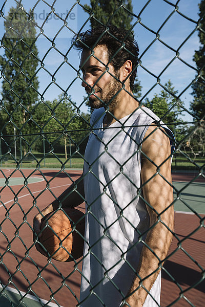 Mann mit Basketball hinter Gitterzaun