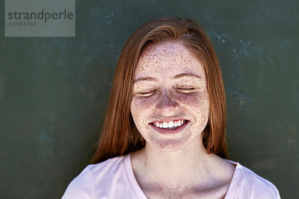 Porträt einer lächelnden jungen Frau mit Sommersprossen  die die Augen schließen.