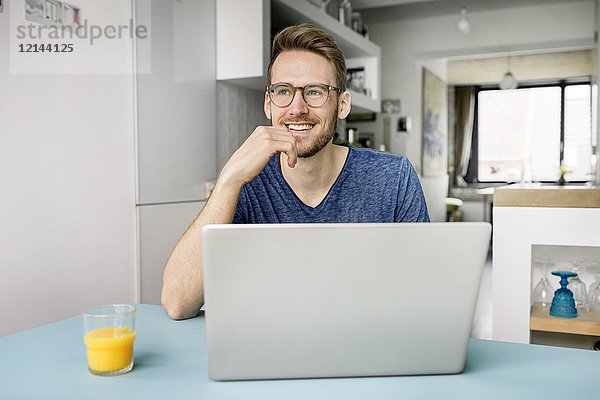 Porträt eines lächelnden Mannes mit Laptop in der Küche zu Hause