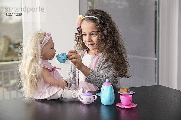 Porträt eines lächelnden kleinen Mädchens beim Spielen mit Puppe und Puppenporzellan-Set