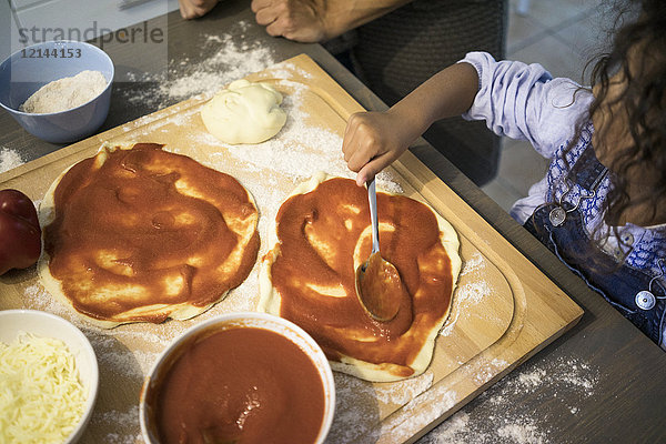 Mädchen in der Küche lernt Pizza backen  Tomatensauce verteilen