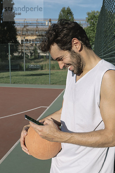 Basketballspieler blickt auf das Smartphone und lächelt