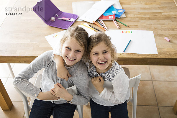 Porträt von zwei glücklichen Mädchen  die sich bei Tisch umarmen