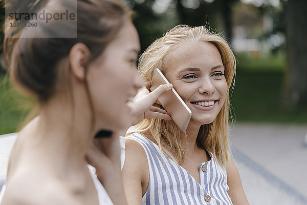 Zwei glückliche junge Frauen mit Handy im Freien