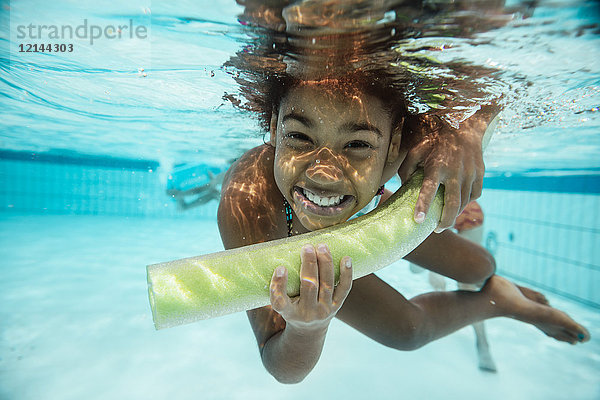 Porträt des lächelnden Mädchens mit Poolnudel unter Wasser im Schwimmbad