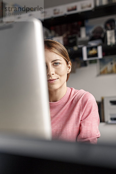 Porträt einer jungen Frau hinter dem Computerbildschirm am Schreibtisch zu Hause