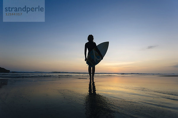 Indonesien  Bali  junge Frau mit Surfbrett am Abend