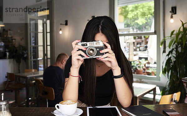 Brünettes Mädchen fotografiert mit ihrer Filmkamera in einem Coffee-Shop