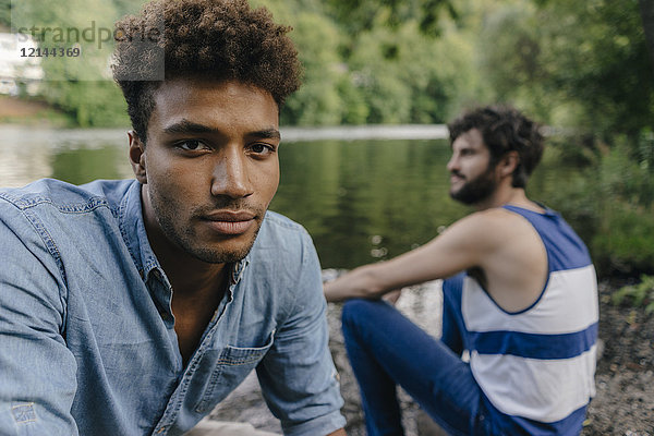 Porträt eines jungen Mannes mit einem Freund  der sich am Wasser entspannt.