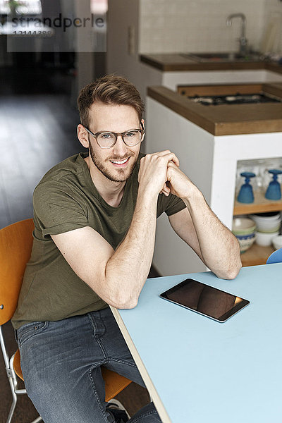 Porträt eines lächelnden Mannes mit Tablette in der Küche zu Hause