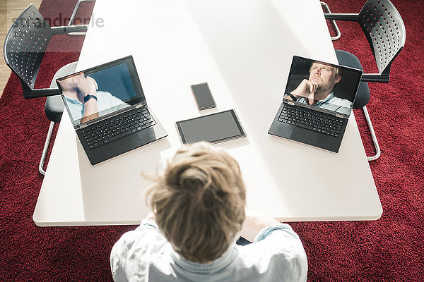 Geschäftsmann mit zwei Laptops  die Bilder von sich selbst zeigen.