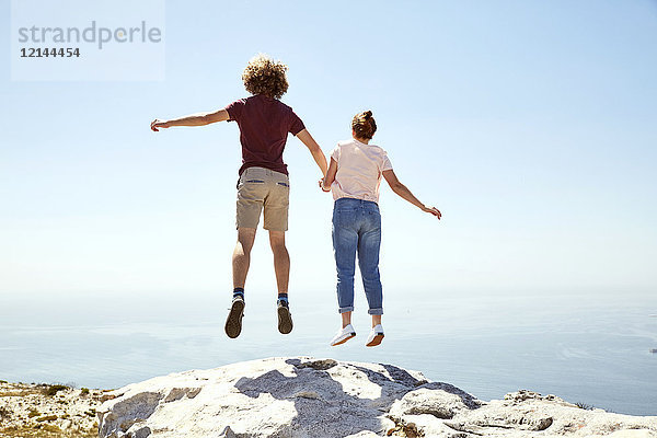 Südafrika  Kapstadt  junges Paar beim Sprung auf einen Berg an der Küste
