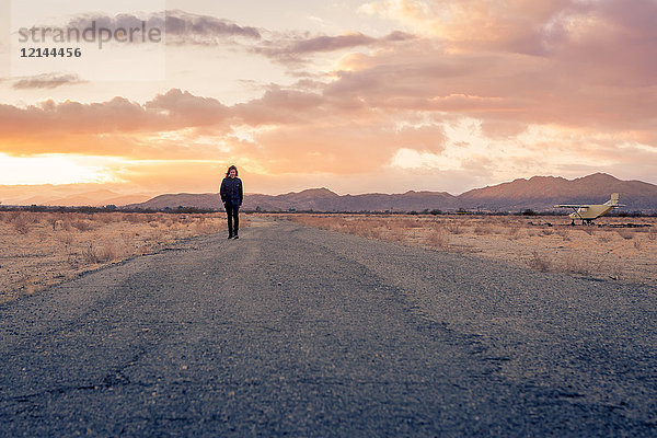 USA  Kalifornien  Joshua Tree  junger Mann geht bei Sonnenuntergang eine Straße entlang.