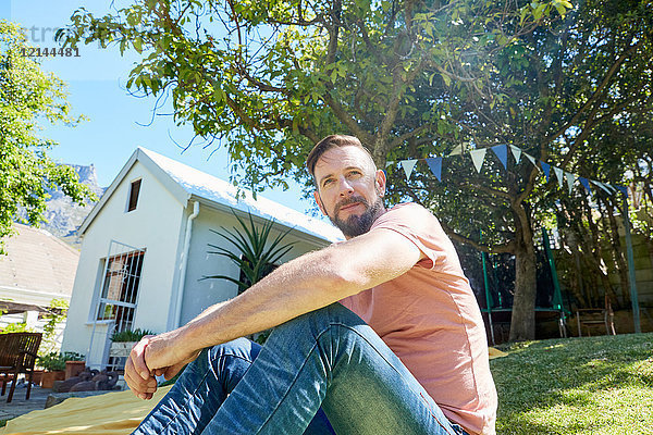 Porträt eines bärtigen Mannes  der vor einem Haus sitzt.