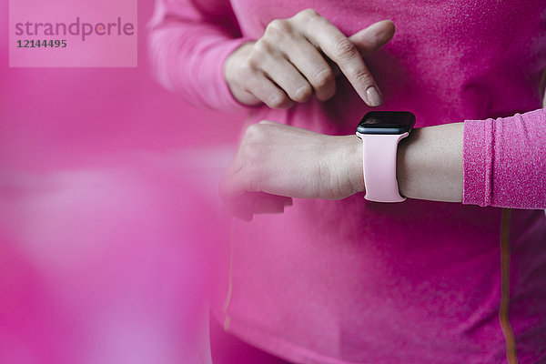 Nahaufnahme einer Frau in rosa Sportbekleidung  die ihre Smartwatch anpasst.