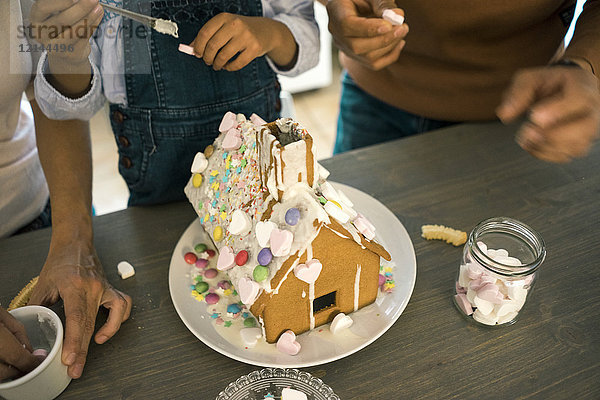 Familie klebt Lebkuchenhaus in der Küche für Weihnachten mit Süßigkeiten