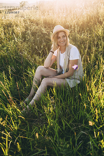 Blonde Frau im Sommer auf der Wiese sitzend