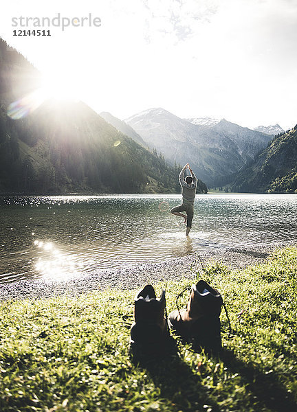 Österreich  Tirol  Wanderschuhe und Mann in Yoga-Pose im Bergsee