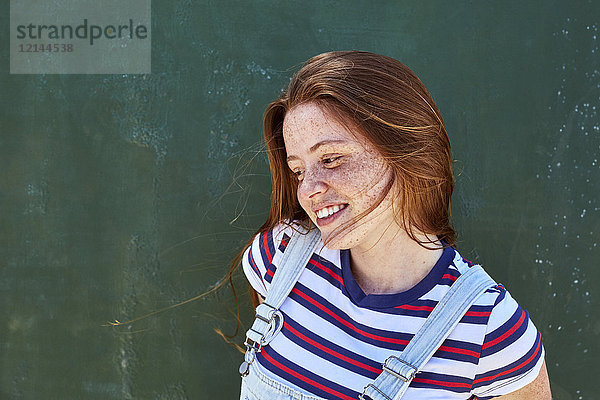 Lächelnde junge Frau mit Sommersprossen vor grüner Wand