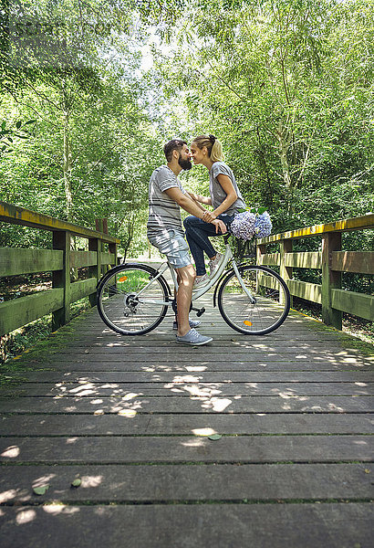 Paar mit Fahrrad  das sich auf einem Holzsteg auf dem Land küssen will.