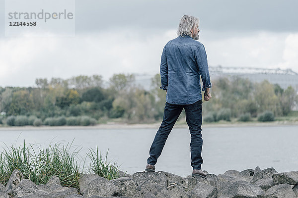 Älterer Mann auf Steinen stehend mit Blick auf den Rhein