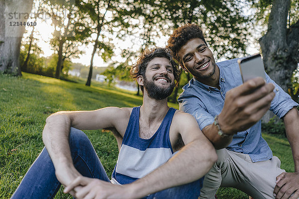 Zwei glückliche Freunde teilen sich ihr Handy im Park.