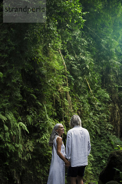 Schöne ältere Frau lächelt Ehemann im tropischen Dschungel an.