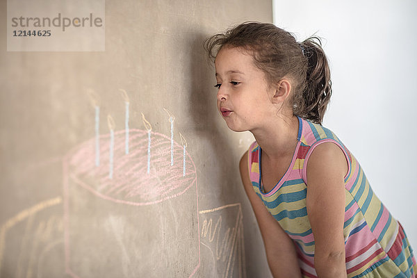 Mädchen  das vorgibt  Kreide auszublasen  Geburtstagskuchen und Kerzenzeichnung auf Betonwand
