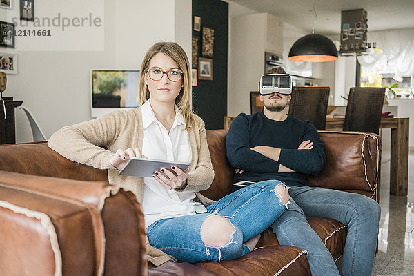 Paar zu Hause auf der Couch sitzend mit Tablett und VR-Brille