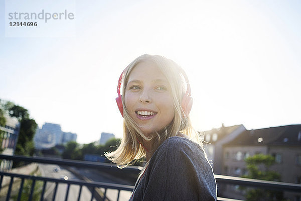 Porträt einer lächelnden jungen Frau im Gegenlicht beim Musikhören mit Kopfhörern
