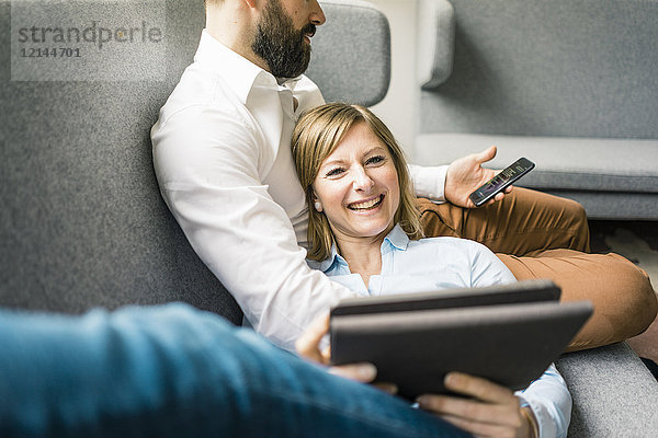 Lächelnde Frau mit Tablette und Mann mit Handy auf Couch