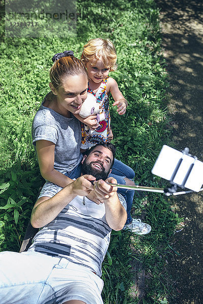 Glücklicher Mann  der auf einer Bank liegt und einen Selfie mit seiner Familie nimmt.