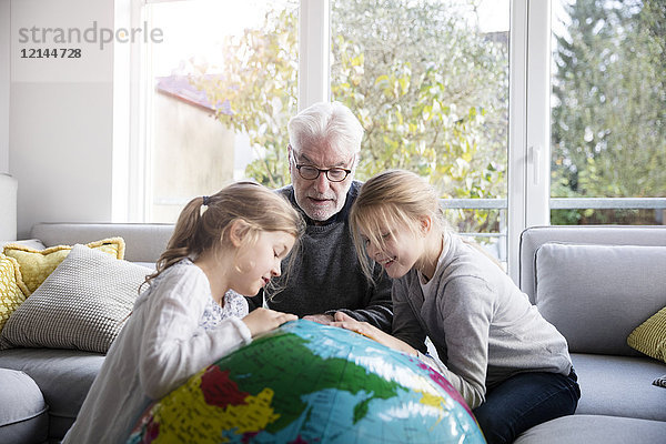 Zwei Mädchen und Großvater mit Globus im Wohnzimmer