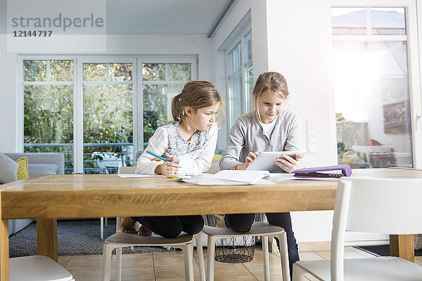 Zwei Mädchen bei den Hausaufgaben am Tisch zusammen mit einer Tablette
