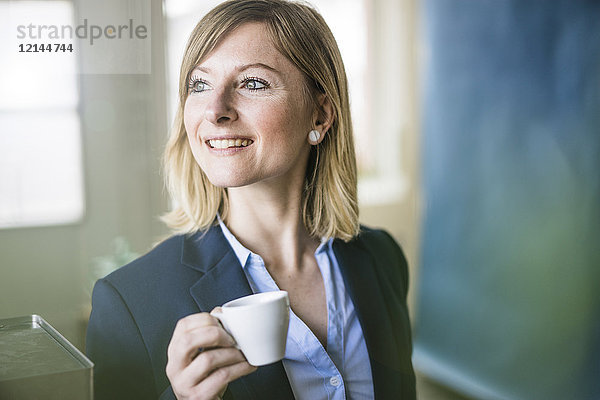Lächelnde Geschäftsfrau mit Espressotasse im Büro