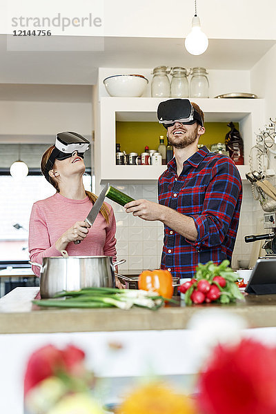 Glückliches junges Paar mit VR-Brille beim gemeinsamen Kochen in der Küche