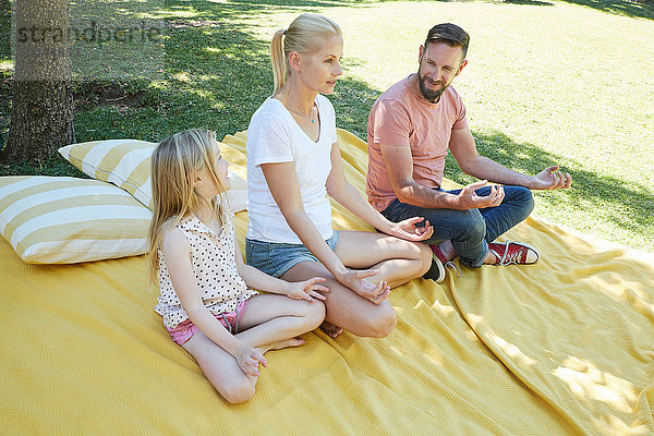 Familie mit einem Mädchen  das Yoga auf einer Decke praktiziert.