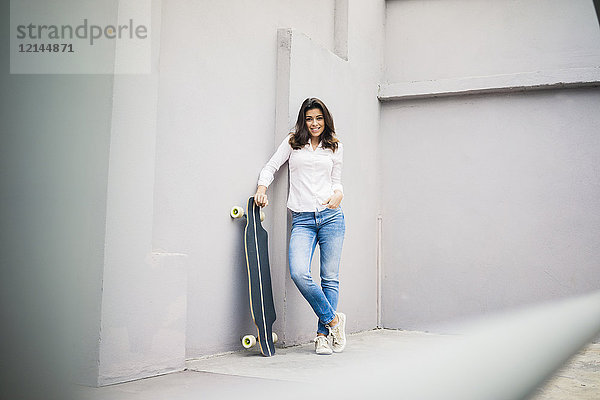 Lächelnde junge Frau mit Skateboard an der Wand lehnend auf der Terrasse