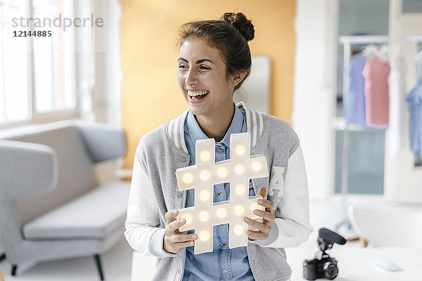 Lachende junge Frau mit Hashtag-Schild im Studio