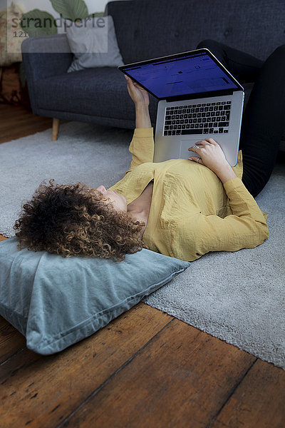 Junge Frau zu Hause auf dem Boden liegend mit Laptop