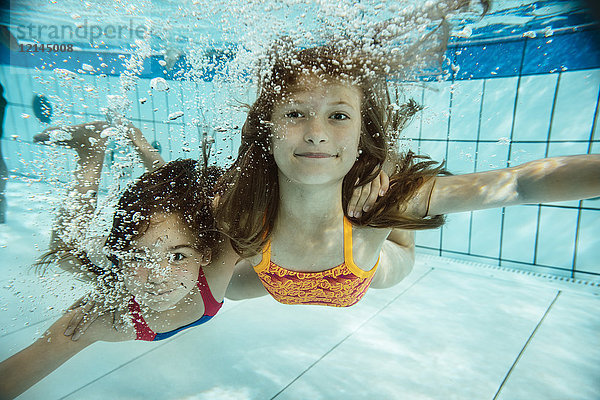 Portrait von zwei unter Wasser schwimmenden Mädchen im Schwimmbad